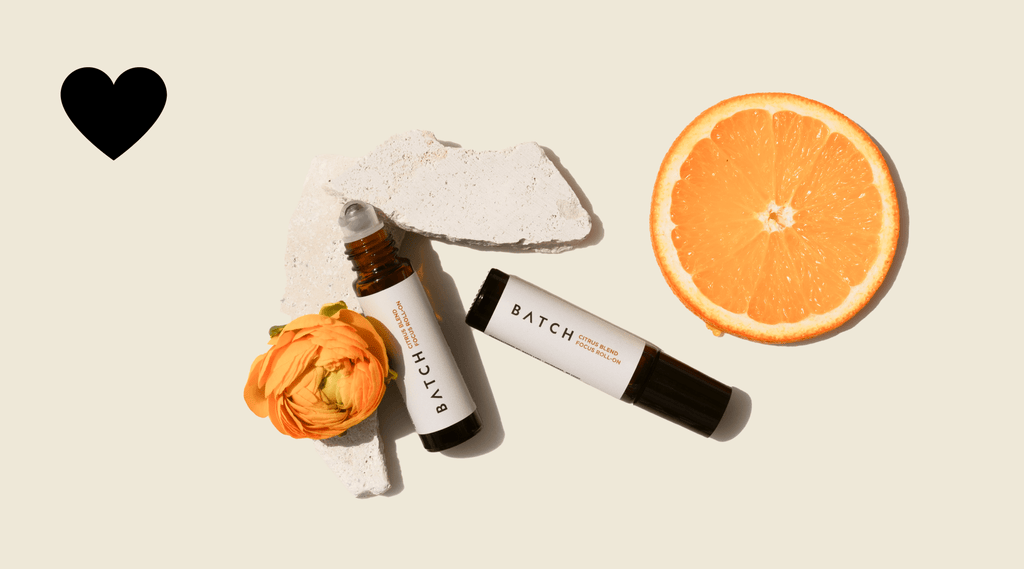 Citrus and rocks with an orange flower next to two roller ball products.